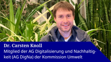 Foto von Dr. Carsten Knoll, der im Schneidersitz vor ein paar Pflanzen sitzt und in die Kamera lächelt, auf seinem Schoß liegt ein geöffneter Laptop