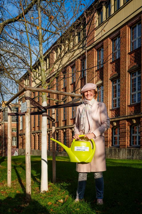 Eine Person steht neben einem Baum und hält eine Mappe in der Hand.