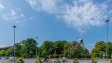 Foto: Zwei Fahrradfahrerinnen auf dem Fritz-Förster-Platz vor dem Beyer-Bau und dem Hörsaalzentrum.