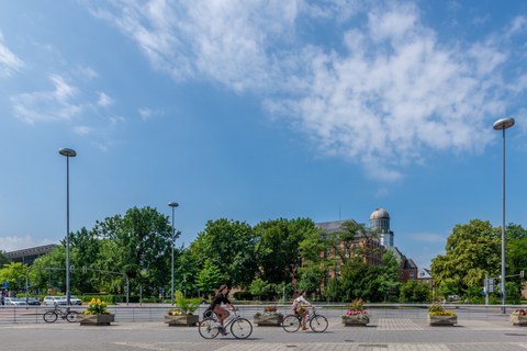 Foto: Zwei Fahrradfahrerinnen auf dem Fritz-Förster-Platz vor dem Beyer-Bau und dem Hörsaalzentrum.