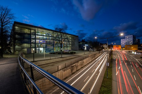 Fotos vom Hörsaalzentrum der TU Dresden am Abend. Im rechten Bildrand sieht man die Straße mit verschwommenen Autolichtern.