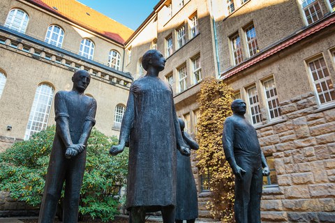 Das Foto zeigt eine Statue. Diese besteht aus fünf Personen, die aufrecht stehen und nach vorn blicken. Die Statue befindet sich bei der Gedenkstätte Münchner Platz.