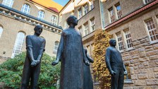 Das Foto zeigt eine Statue. Diese besteht aus fünf Personen, die aufrecht stehen und nach vorn blicken. Die Statue befindet sich bei der Gedenkstätte Münchner Platz.