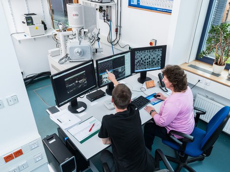 Das Foto zeigt zwei Personen vor mehreren Computerbildschirmen. Auf den Bildschirmen sind Ergebnisse von Bodenproben zu erkennen. Die Personen reden miteinander und werten die Proben aus. 
