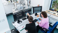 Das Foto zeigt zwei Personen vor mehreren Computerbildschirmen. Auf den Bildschirmen sind Ergebnisse von Bodenproben zu erkennen. Die Personen reden miteinander und werten die Proben aus. 