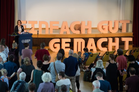 Mehrere Menschen hören einem Vortrag zu. Auf dem Redner:innenpult stehen große Buchstaben "Einfach gut gemacht".