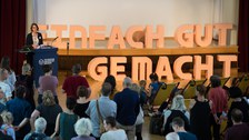 Mehrere Menschen hören einem Vortrag zu. Auf dem Redner:innenpult stehen große Buchstaben "Einfach gut gemacht".