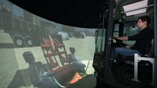 Foto: Mann sitzt in einem Simulator zur Nachbildung des Fahrverhaltens einer Baumaschine und bedient diesen. 