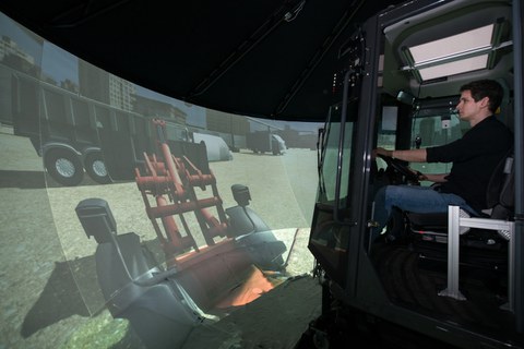 Foto: Mann sitzt in einem Simulator zur Nachbildung des Fahrverhaltens einer Baumaschine und bedient diesen. 