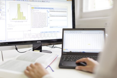 Es ist ein Buch zu sehen und zwei Bildschirme, auf denen SPSS Daten angezeigt werden.