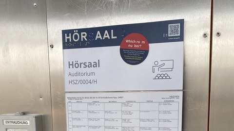 An Profil- und Brailleschrift beschädigtes Türschild vom Hörsaal 4