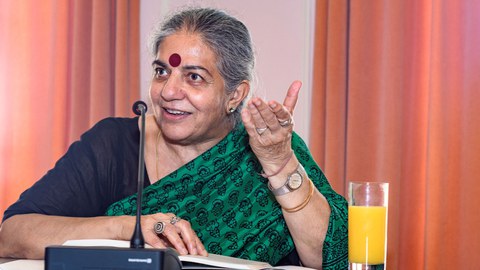 Dr. Vandana Shiva sitzt an einem Tisch und spricht.