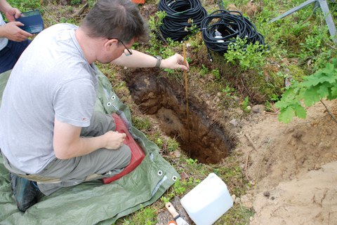 Mann sitzt auf einer Wiese mit Messinstrumenten vor einem größeren Loch.