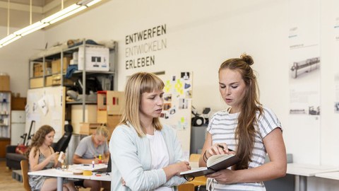 Zwei Studentinnen besprechen in einer Werkstatt Aufzeichnungen.