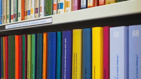 Blick auf ein weißes Bücherregal mit bunten, schmalen Büchern.