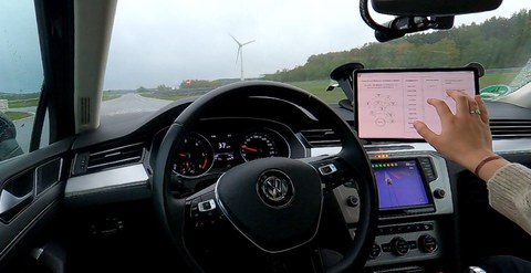Blick in ein Auto-Cockpit, eine Hand bedient einen Bildschirm.