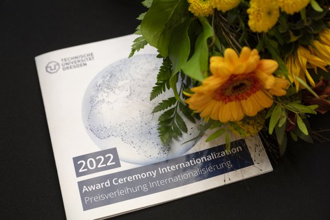 Fotoaufnahme eines Programmheftes zur Verleihung des Preis Internationalisierung sowie eines Blumenstraußes am rechten Bildrand.