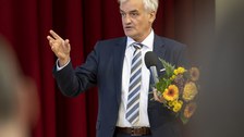 Foto des Preisträgers Prof. Stamm vom ABCD-Centre, der in ein Mikrofon spricht und einen Blumenstrauß in den Händen hält.