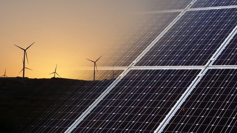 Rechts im Bild Solarpanele, links Windräder vor einem Abendhimmel