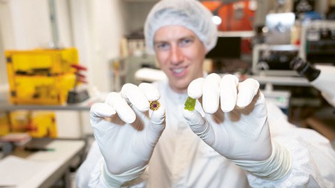 Ein Mann in Schutzkleidung zeigt ein Gummibärchen und einen Sensor.