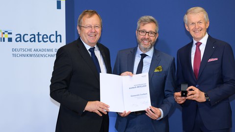 Drei Herren, in der Mitte Prof. Cuniberti, bei der Übergabe einer Urkunde.
