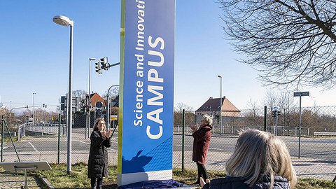 Three women are applauding before an unveiled column.