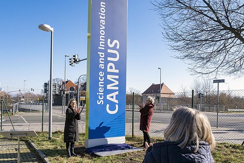 Three women are applauding before an unveiled column.