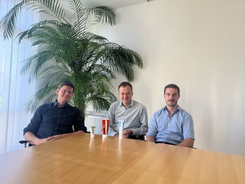 3 junge Männer sitzen an einem Tisch. Vor Ihnen drei Tuben mit Handseife.