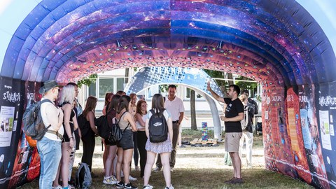 Eine Gruppe von Menschen steht in einem Pavillon, an dessen Decke das Weltall abgebildet ist.