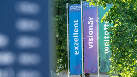 Drei Banner vertikal an einem Mast mit der Aufschrift Exzellent, Visionär, Weltoffen