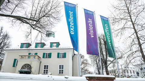 Verschneites Rektorat der TU Dresden, davor 3 Banner: Exzellent, Visionär, Weltoffen