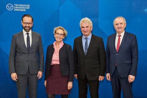 Gruppenfoto mit vier Personen, drei Männer und eine Frau vor blauem Hintergrund und TUD-Logo