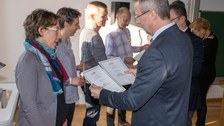 Mehrere Personen bekommen eine Urkunde überreicht.
