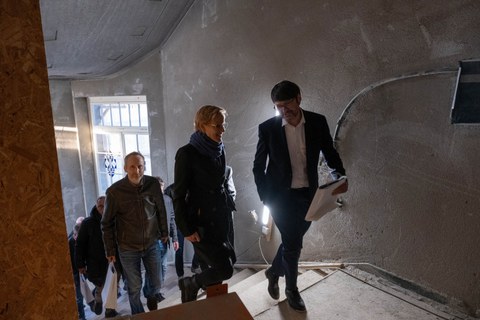 Mehrere Personen gehen auf einer Baustelle in einem GEbäude eine Treppe hinauf.