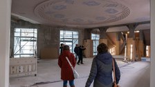 Mehrere Personen sehen sich auf einer Baustelle in einem Gebäude eine runde Deckenverzierung an.