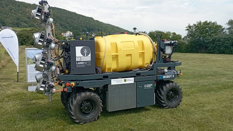 Graues Gefährt mit dicken Rädern und grauen Aufbauten mit den Schrifzügen und Logos v.l. Landnetz, Freistaat Sachsen, TU Dresden. Daraun eine gelber Tank. Hinten ein silberfarbenes Gestell mit 5 übereinander angebrachten runden Bauteilen.