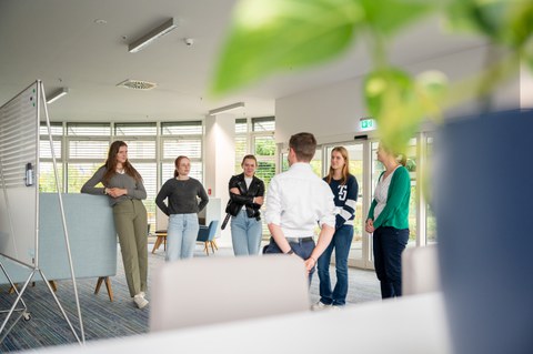Fotoaufnahme von sechs Personen, die in einem großzügigen Büro stehen und einander zugewandt sind.
