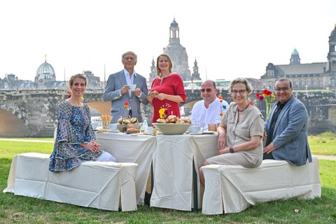 Foto von Maria Noth, Prof. Gerhard Ehninger, Dr. Eva Sturm, Ronald Zenker, Prof.in Ursula Staudinger und Raafat Saeed (v. l. n. r.) an einer Tischgarnitur auf den Elbwiesen vor der Dresdner Altstadtkulisse.