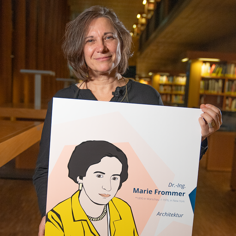 Porträtaufnahme einer Frau, die ein Schild in die Kamera hält, das ein gezeichnetes Porträt von Marie Frommer zeigt.