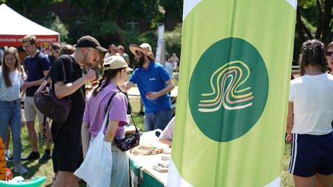 Menschen stehen an einem Infostand. Im Vordergrund ist eine Fahne mit dem Logo der TU-Umweltinitiative tuuwi
