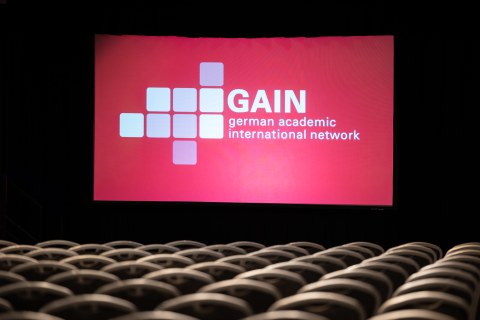 Fotoaufnahme eines projeziierten Bildes, das die GAIN-Konferenz ankündigt.