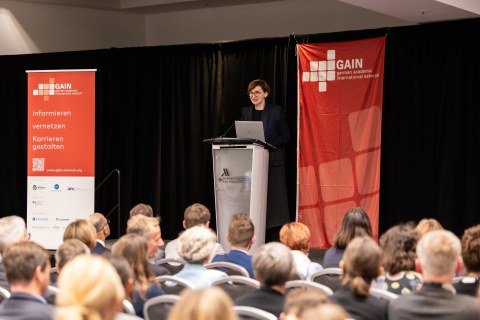 Foto von Bettina Stark-Watzinger, die auf einer Bühne an einem Pult zu Publikum spricht.