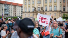 Fotoaufnahme von Veranstaltungsteilnehmenden auf dem Dresdner Altmarkt. Eine Frau hält ein Transparent ins Bild mit dem Schriftzug Demokratie und einem Herz.