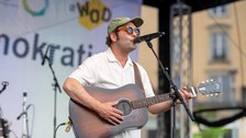 Nahaufnahme des Musikers Bosse auf einer Bühne am Mikrofon mit Gitarre.