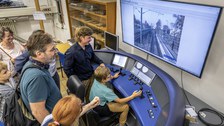 Fotoaufnahme eines Jungen, der an einem Eisenbahnsimulator sitzt. Um ihn herum stehen weitere Personen und schauen zu.