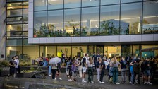 Fotoaufnahme von Menschen, die vor einem Gebäude mit einer großen Fensterfront stehen.