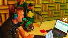 Foto von einem Mann, der an einem Laptop sitzt und Kopfhörer trägt.