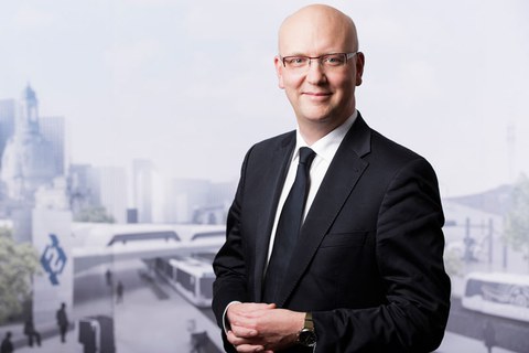 Portrait Prof. Niels Modler im Anzug vor einer Wand mit einer unscheinbaren, futuristischen Stadtszene aus Zügen, Bussen, Hochhäusern und der Frauenkirche.