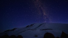 Ein riesiger Himmel voller Sterne über der dunklen Silhouette der Landschaft.