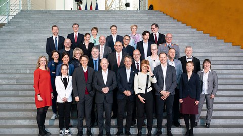 Gruppenbild auf einer Treppe. In der ersten Reihe Bundeskanzler Scholz.